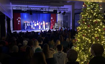 En gruppe mennesker i et rom med et juletre og en scene