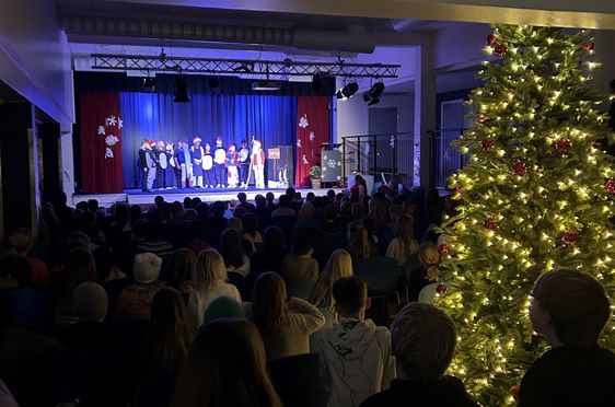 En gruppe mennesker i et rom med et juletre og en scene